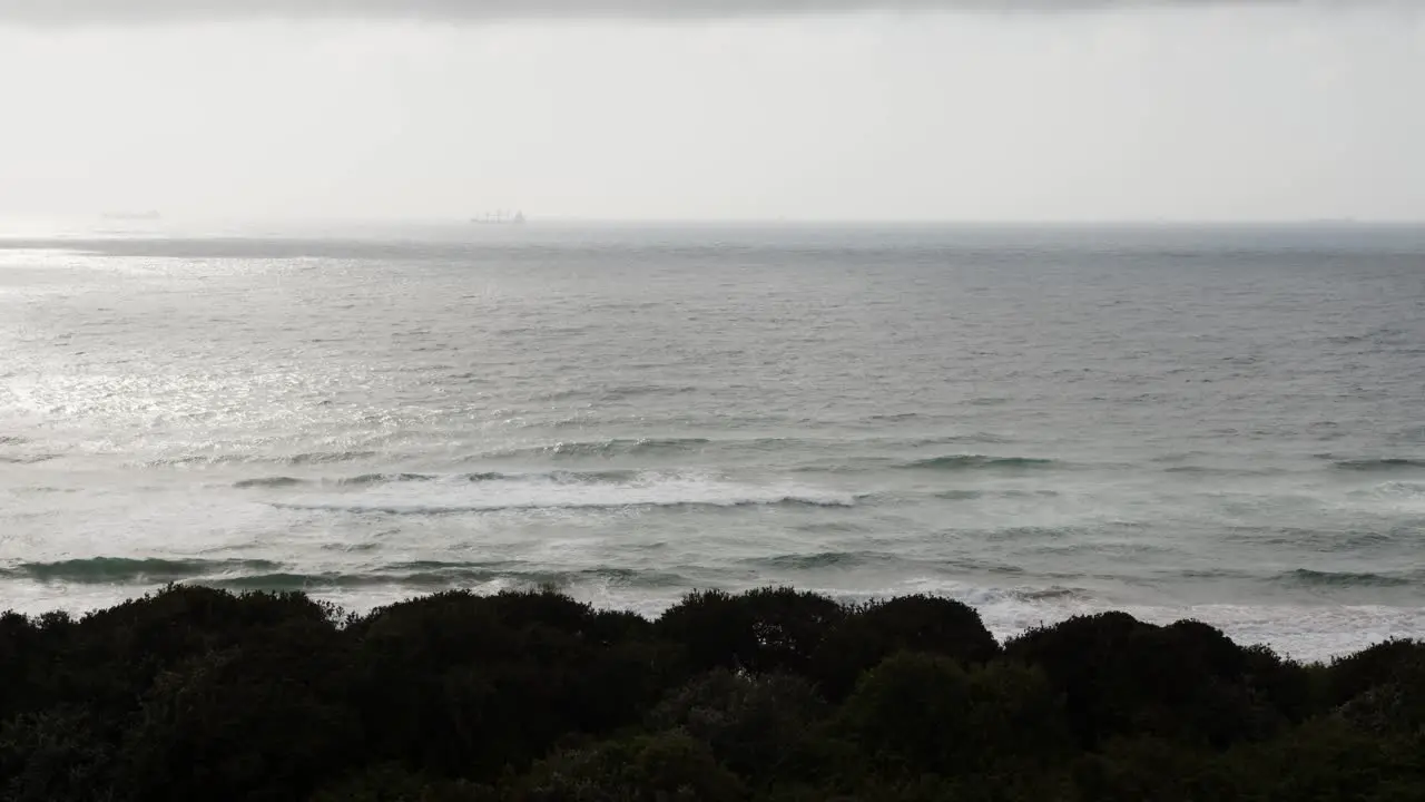 A long shot of waves coming onto a dark beach with a ship just barely visible in the distance