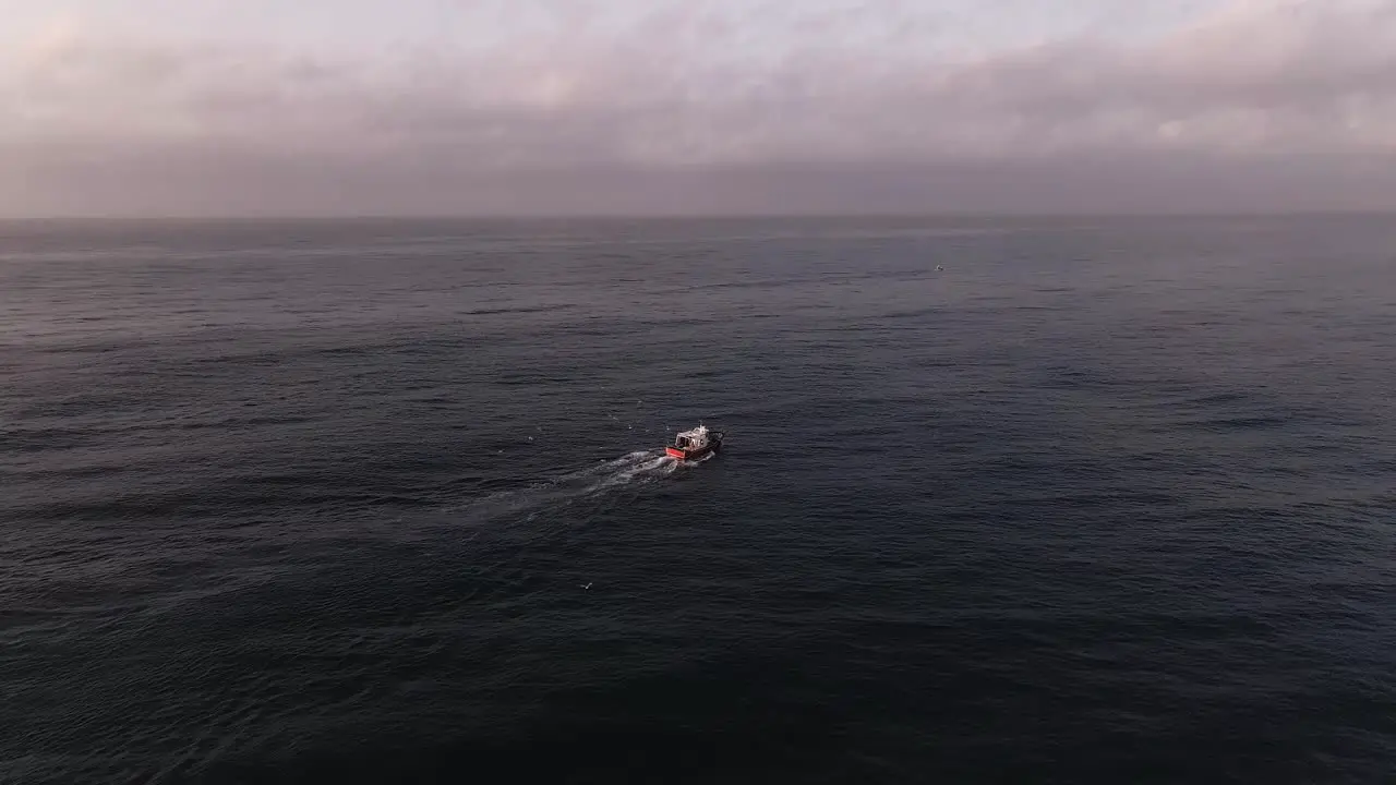 Aerial view flying towards fishing boat on quiet ocean waves cloudy sunset seascape