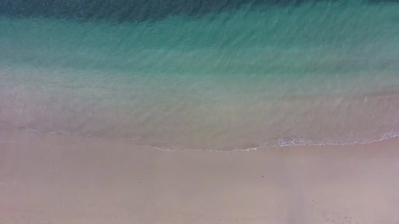 Static aerial top down shot of blue turquoise sea shore water while waves break quietly