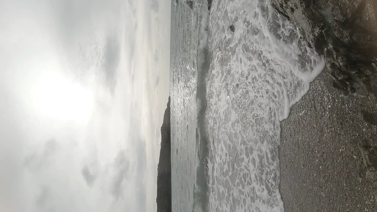 VERTICAL slow motion ocean waves crashing in harmony against rock coastline at sunrise