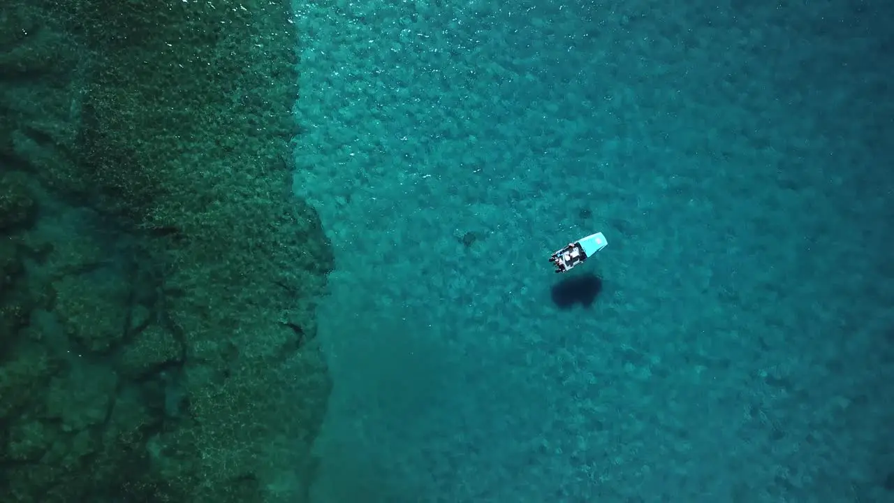 Static aerial view of a boat floating on crystal clear blue water above a beautiful coral reef