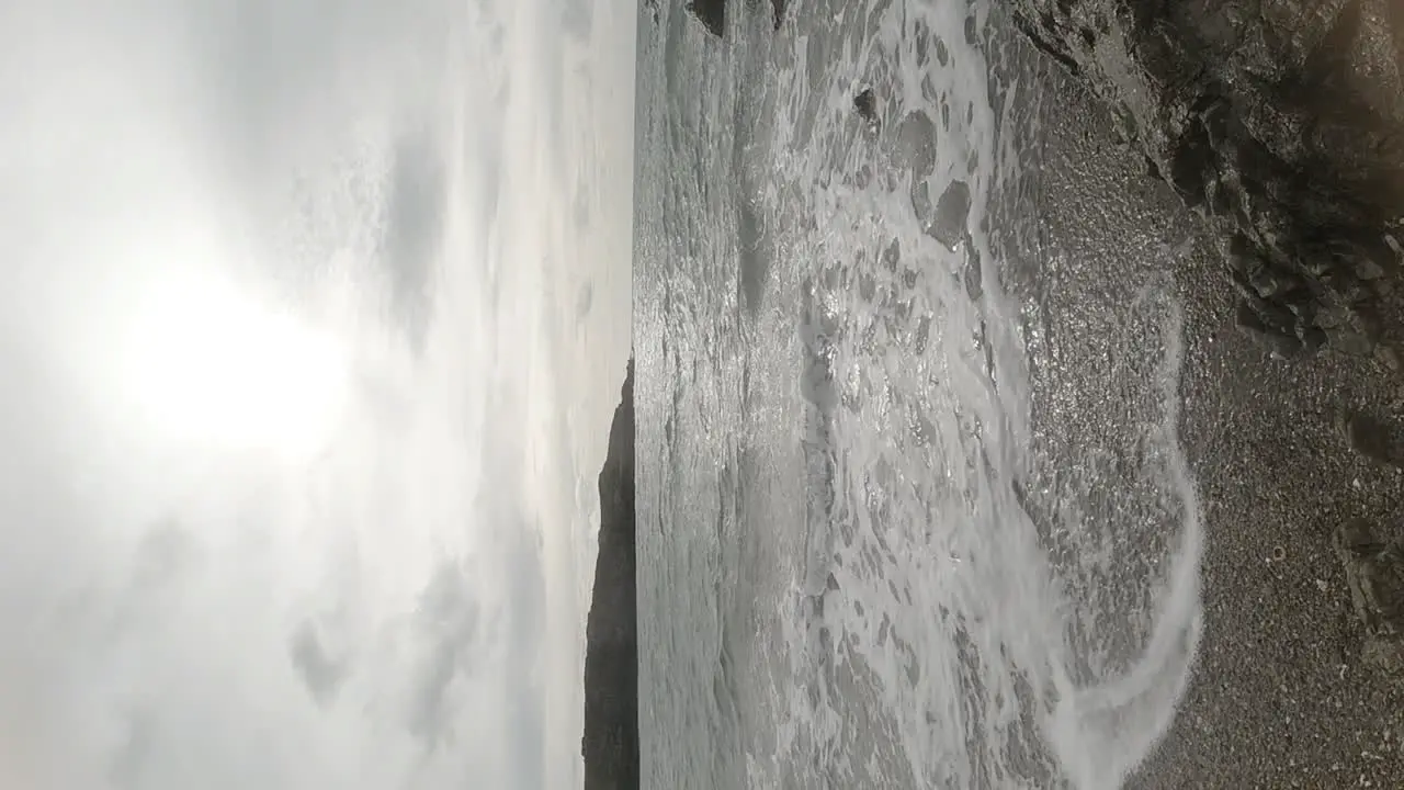 VERTICAL slow motion ocean waves crashing against idyllic rock coastline at sunrise