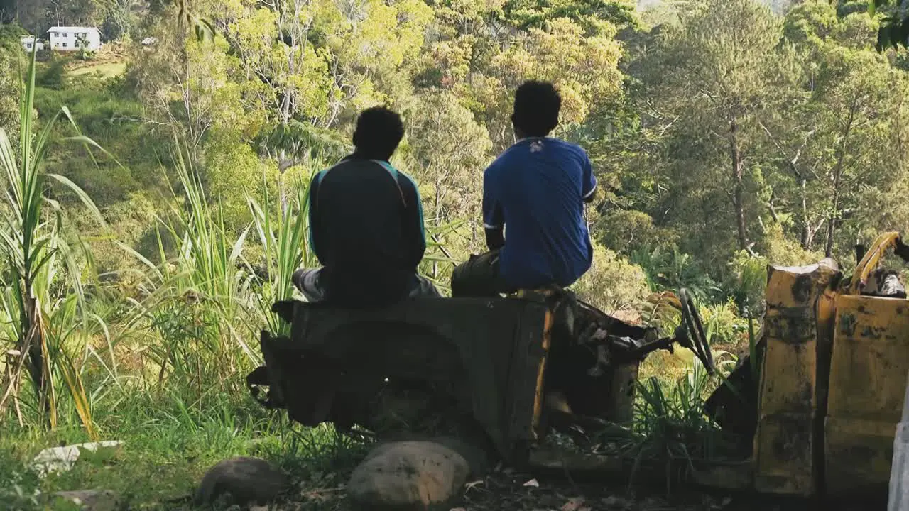 Two male sitting on an old damage car starring into the mountains and valley