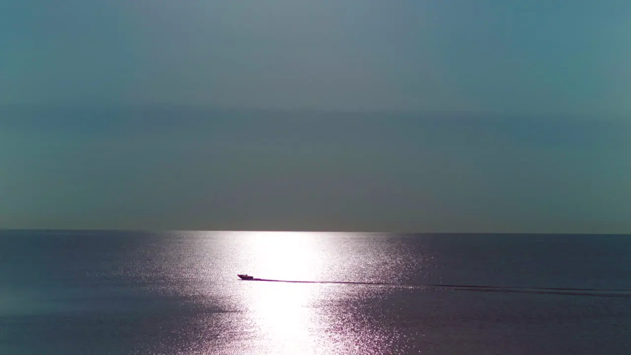 A boat moving on the water going through sunlight during sunrise