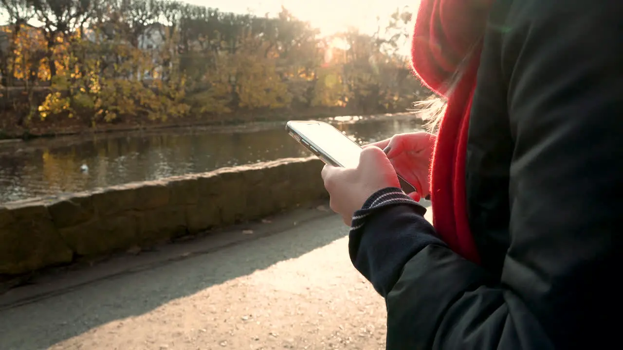 Close up of female person typing on smartphone outdoors beside river during sunset in background 4K