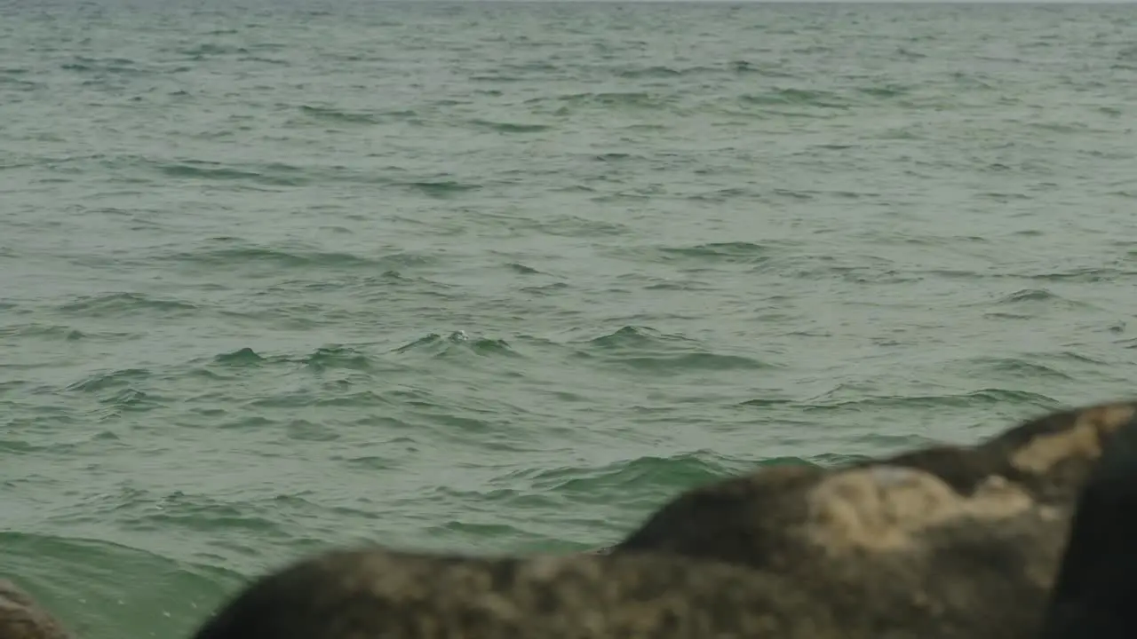 Slow motion of rippling sea water with rocks in foreground