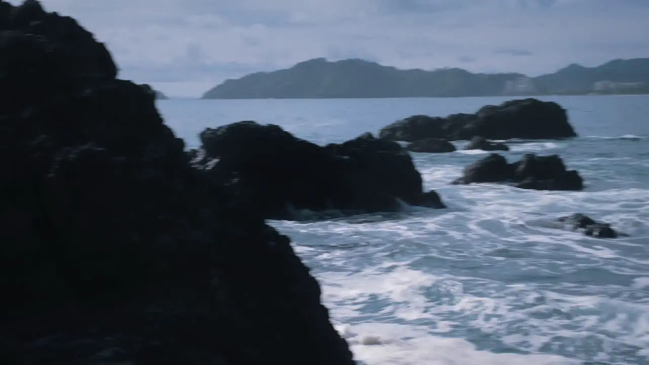 Waves crashing against the large black rocks by the coast