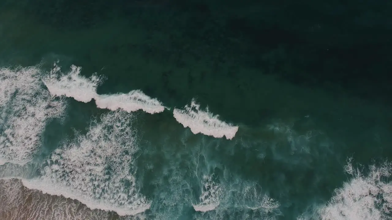 Birds eye view of beautiful clear blue waves rising drone shot