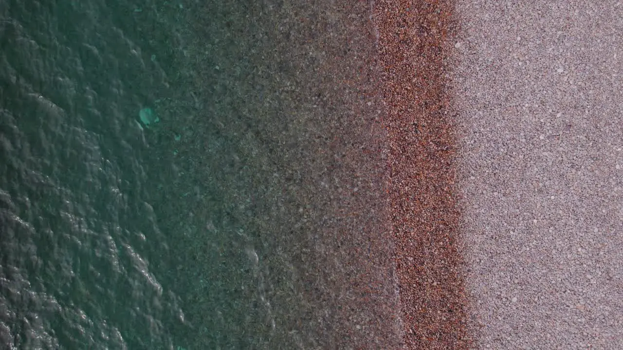 Aerial top down slow motion drone shot of the sea on a sunny day on a pebble beach Weymouth Dorset UK