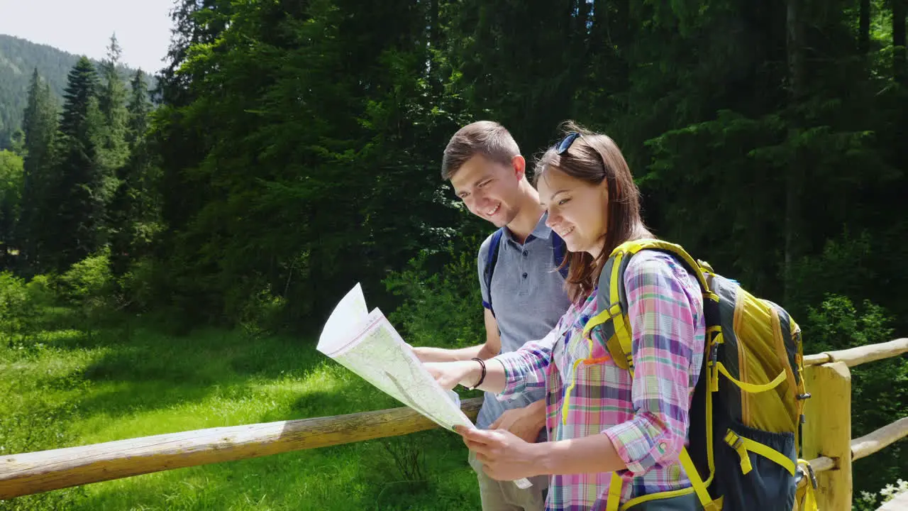 Tourism And Active Lifestyle A Young Couple Looks At The Map Stand In A Picturesque Place On A Summe