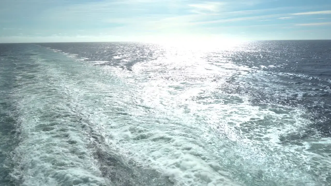 The wake from the rear of the cruise ship in the open ocean with the reflection from the sun off the water