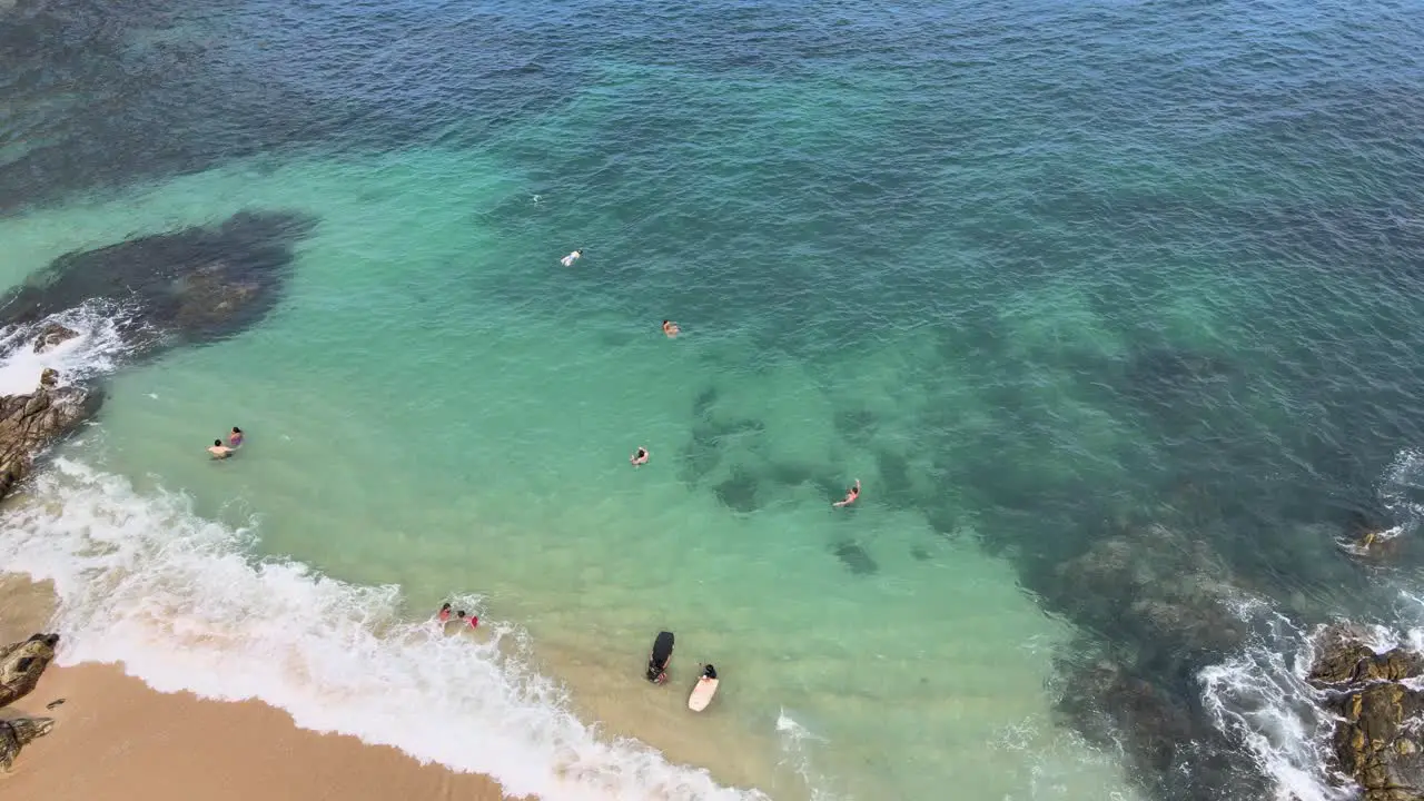 Jib down and tilt up approaching a small beach with people swimming at a sunny day