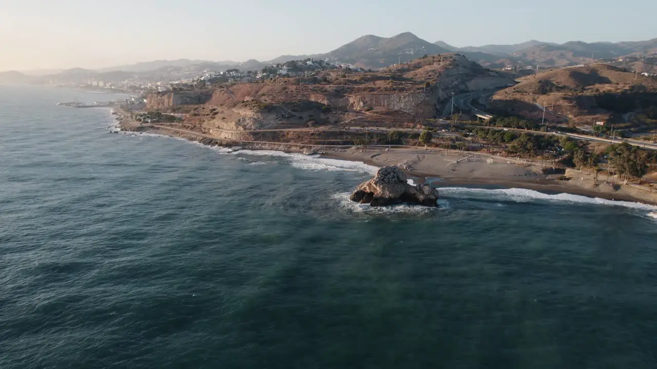 Cinematic aerial zoom in on the famous Raven Rock of El Peñón del Cuervo that splits the bay into two beaches on the coast of the Alboran Sea in Malaga Spain