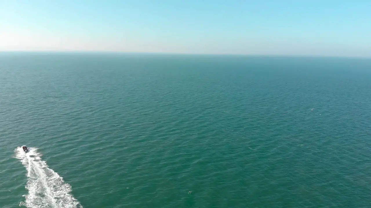 Cinematic aerial drone shot of speedboat sailing into distance across deep blue sea on english coastline on sunny summers day with clear blue sky