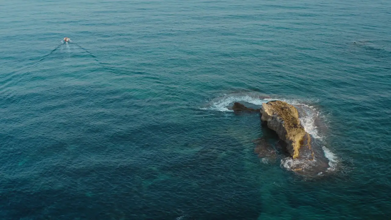 Boat passing a stone ridge in a bright blue sea