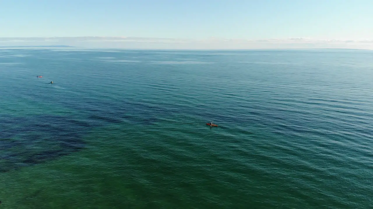 High aerial orbit around a kayaker in the middle of the calm blue sea