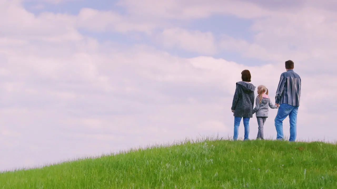 A Family Of Three People Father Mother And Daughter 6 Years Old Stand On Top Of A Green Hill