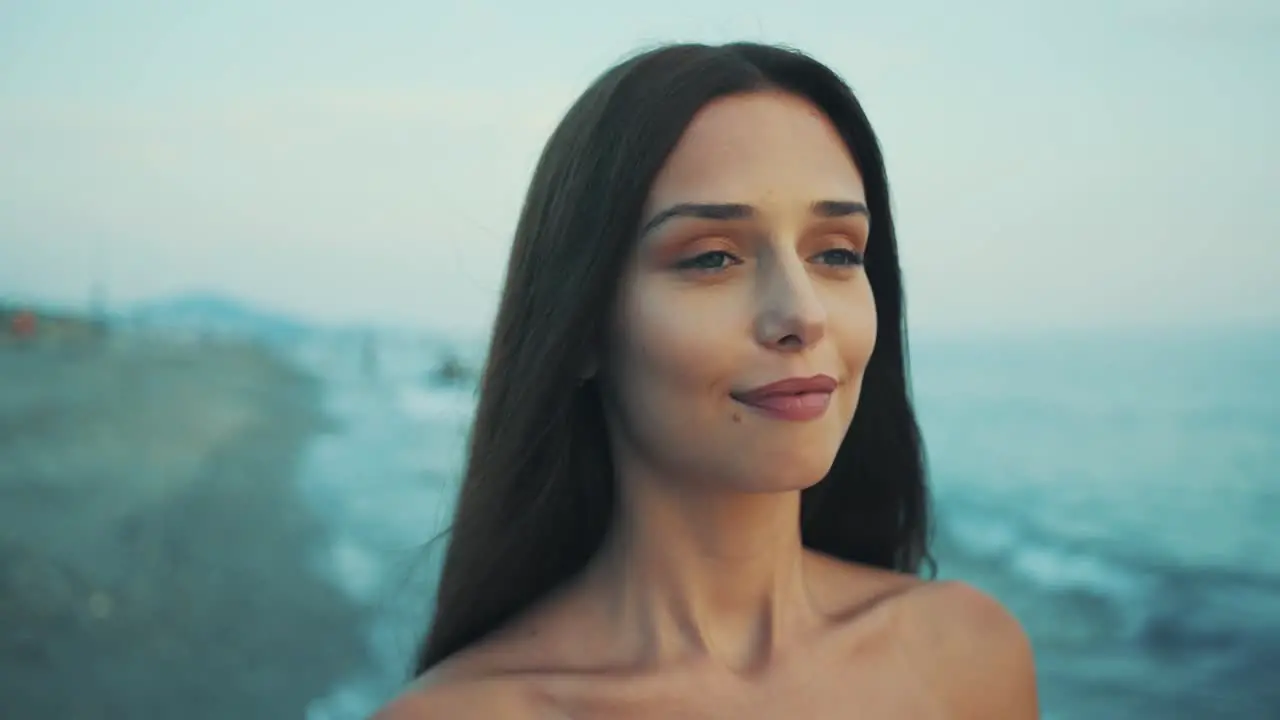 The camera captures the face of young girl walking on the beach at sunset