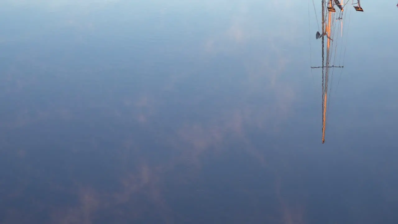 A mast reflects in the water at a harbor in this artistic shot