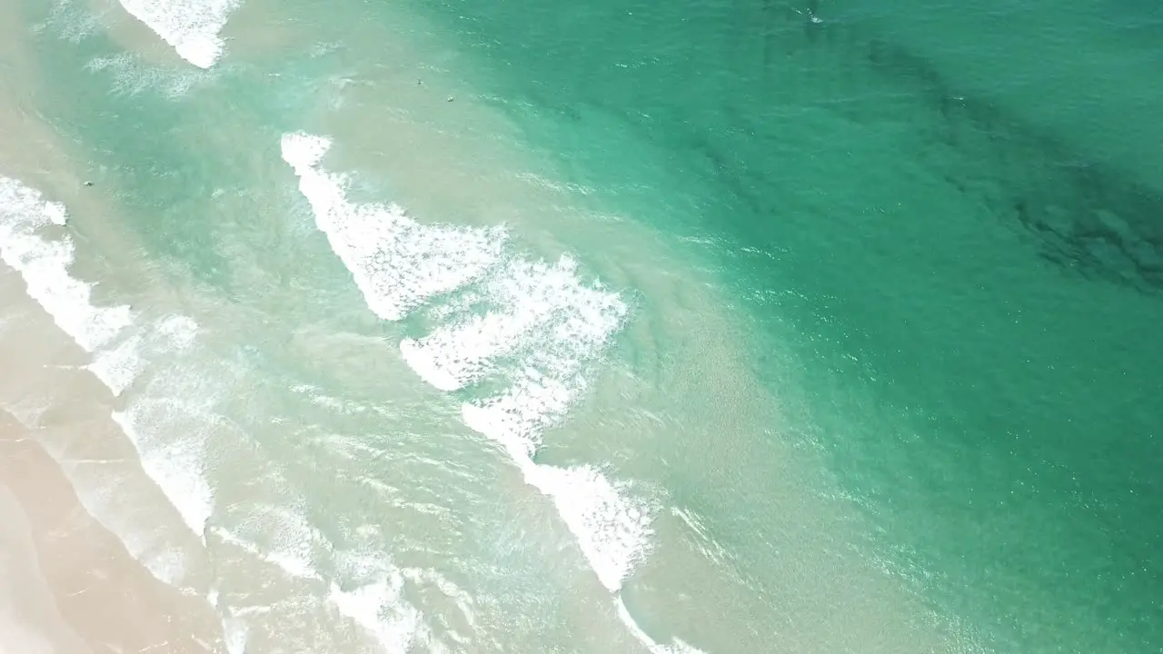 Drone aerial panning up from beautiful blue beach with white sand to forest and lighthouse