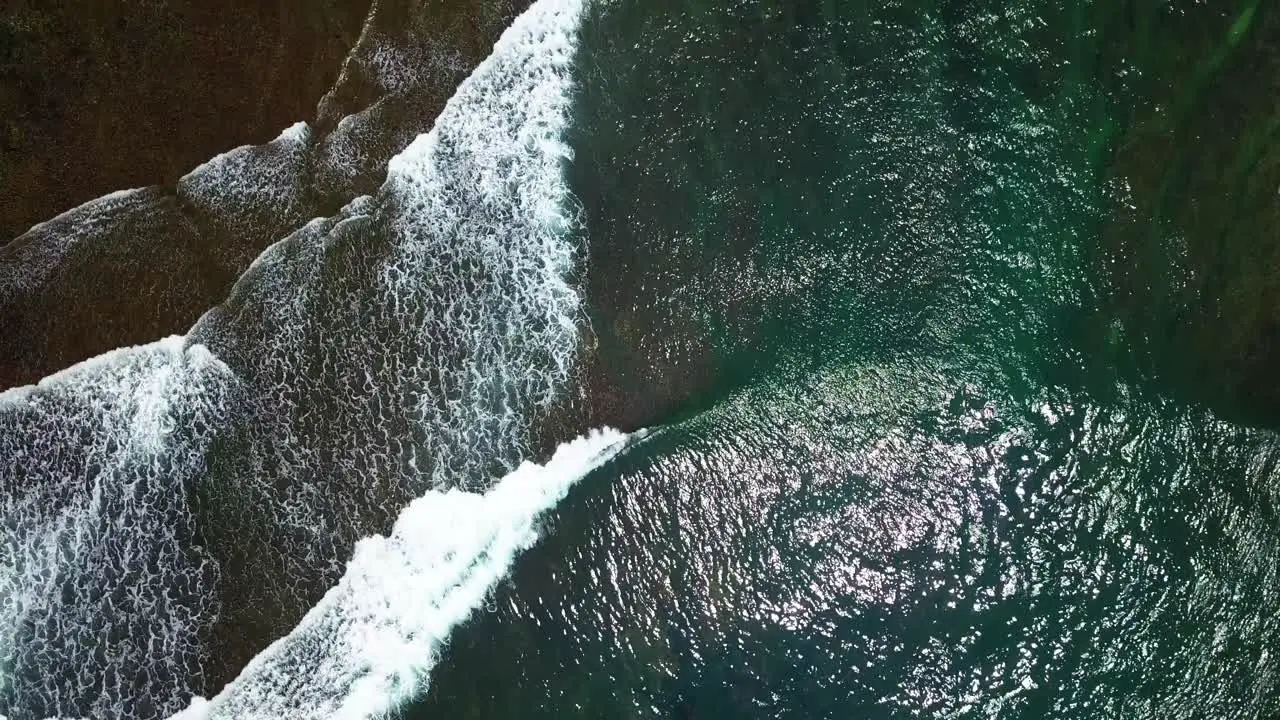 Overhead drone shot of beach waves with clear water and visible the coral rocks