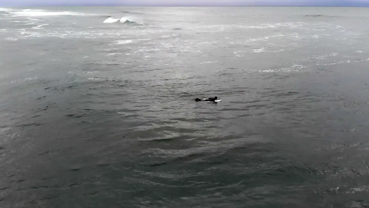 drone flying around surfer paddling out into ocean