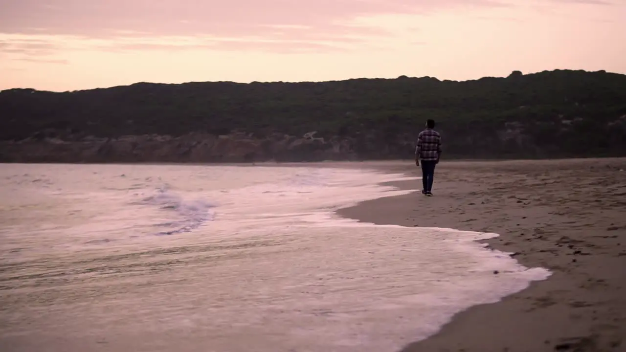 Slowmotion shot of a man walking alongside the ocean during sunset