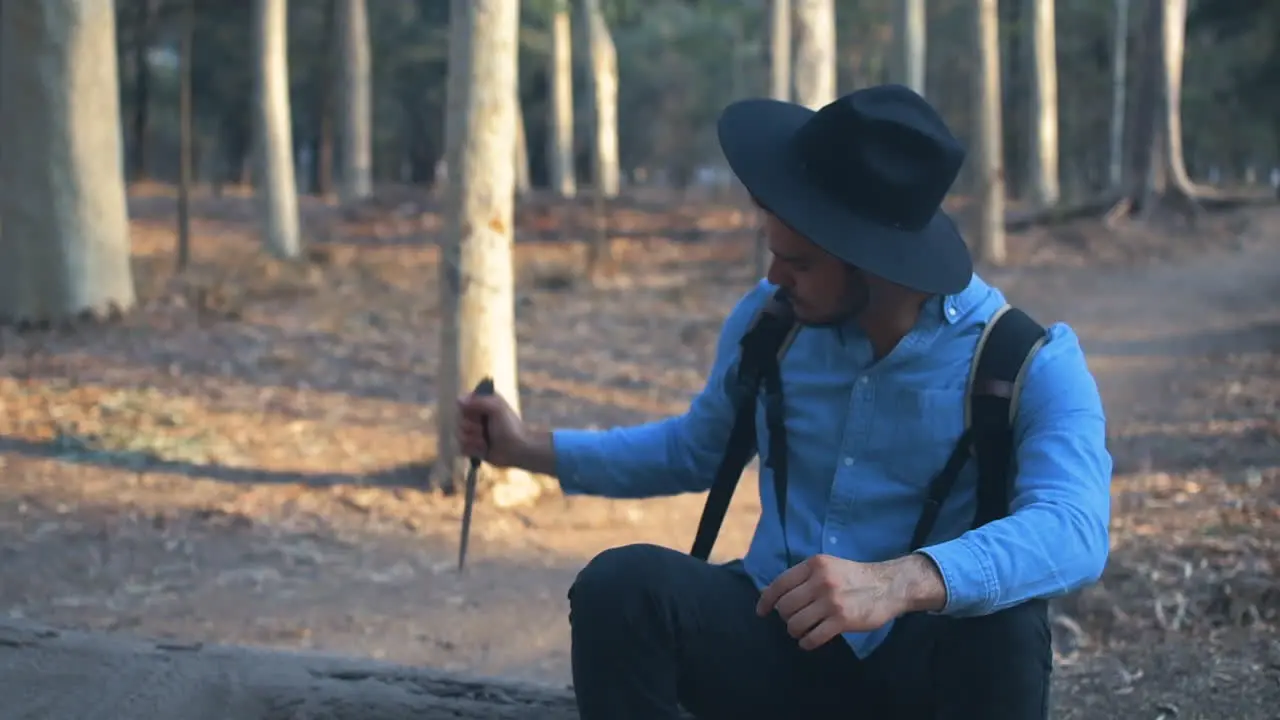 Explorer sticking a knife unto a log and contemplating nature