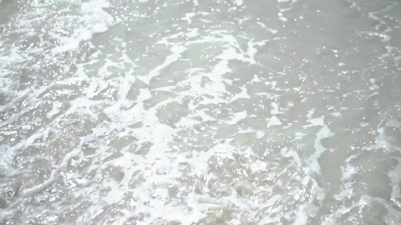 Waves washing small rock and sand with daylight reflection