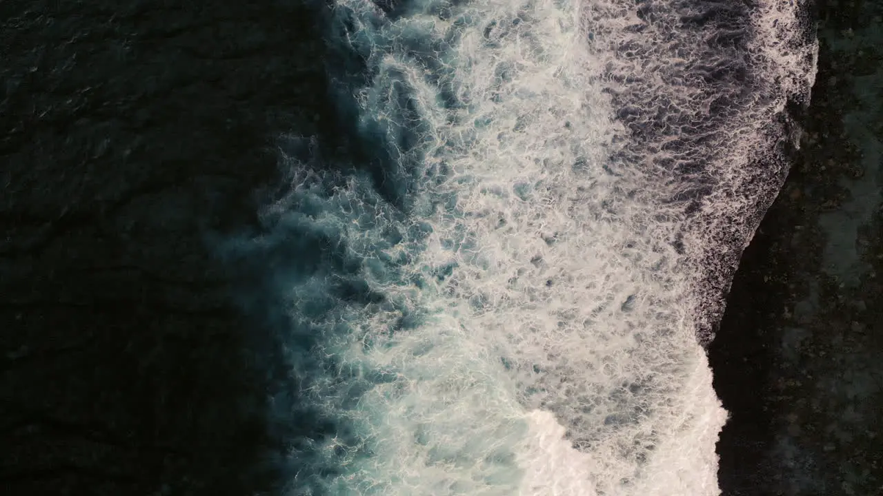 Aerial birds eye view of dramatic dark moody ocean water with white foaming waves breaking