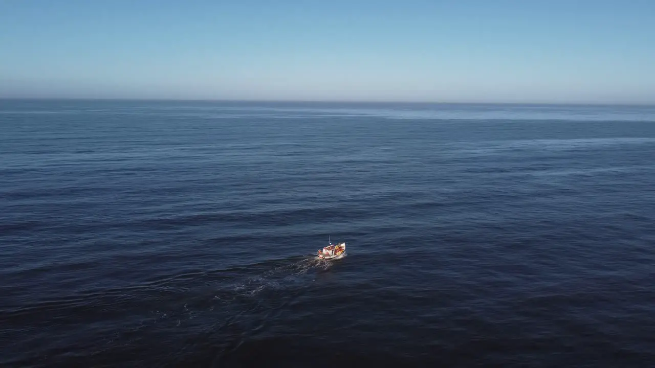 Aerial view of a small boat in the middle of a calm and immense sea sailing towards the horizon