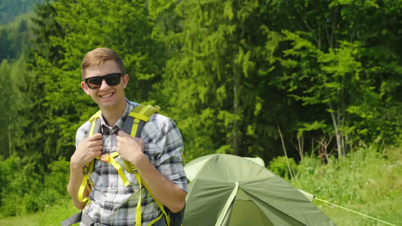 A Young Man With A Backpack Is Looking At The Camera Standing In The Background Of A Camping Tent Po