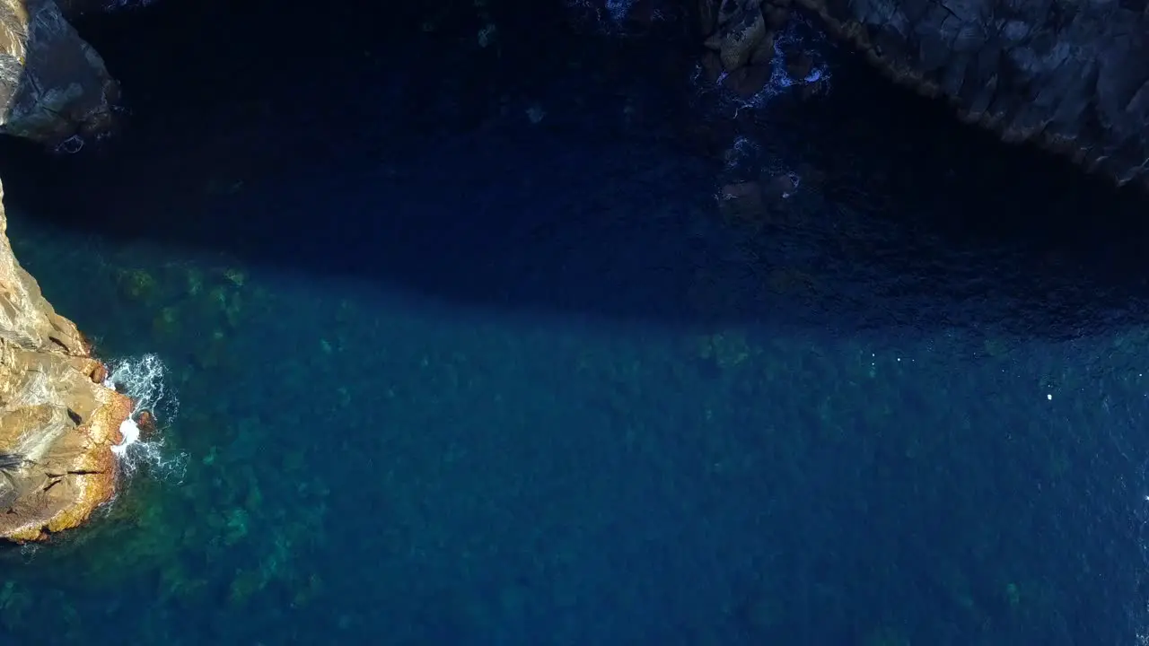 Drone ascent revealing coastal rocky cliffs with crystal sea water below in volcanic Sao Miguel island Azores