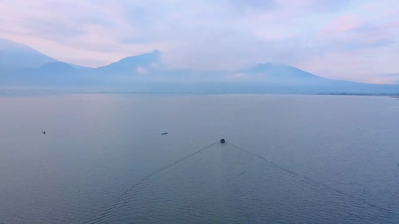 Drone footage of a boat that is sailing on a huge lake with mountains on the background Rawa Pening Lake Indonesia