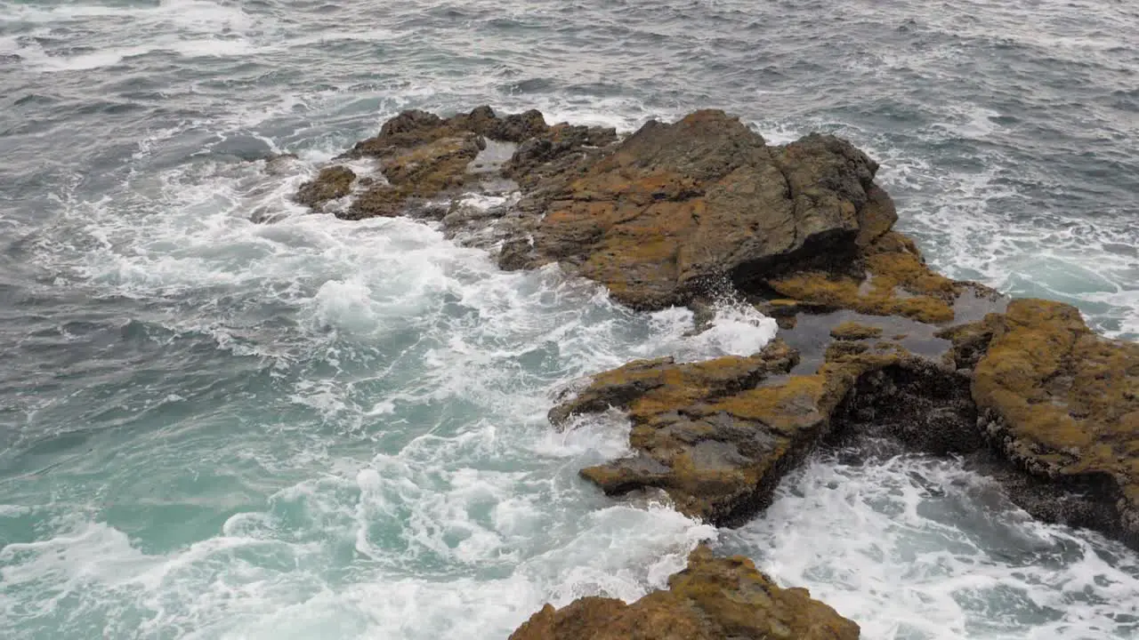 Slow motion wide shot of ocean waves crashing on rocking shore