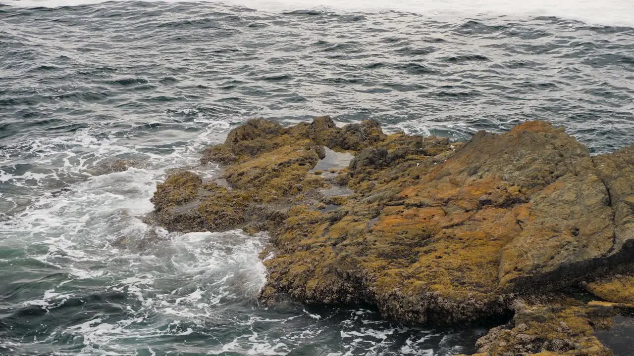 Slow motion medium shot of ocean waves crashing on rocking shore