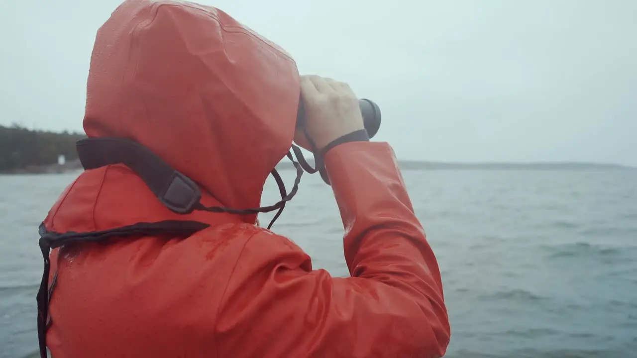 Man in red raincoat looking trough binoculars in storm