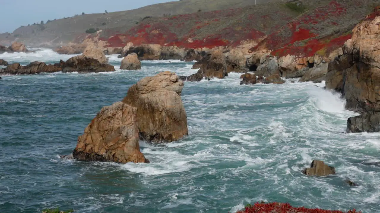 Medium shot of Large waves crashing against jagged Big Sur Coastline in Garrapata wih 2 large rocks in foreground in Slow Motion