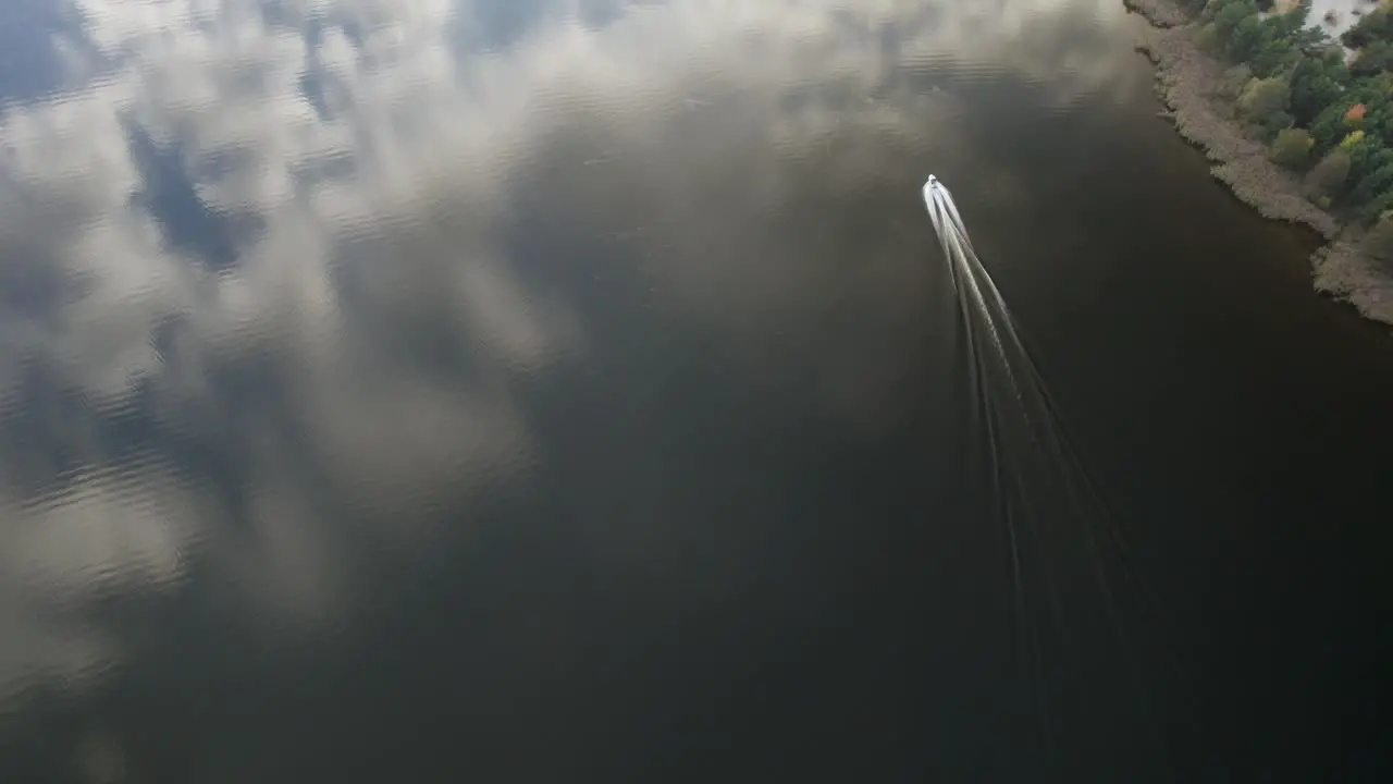 Aerial high altitude shot of the motorboat riding fast on the calm dark waters in northern Europe