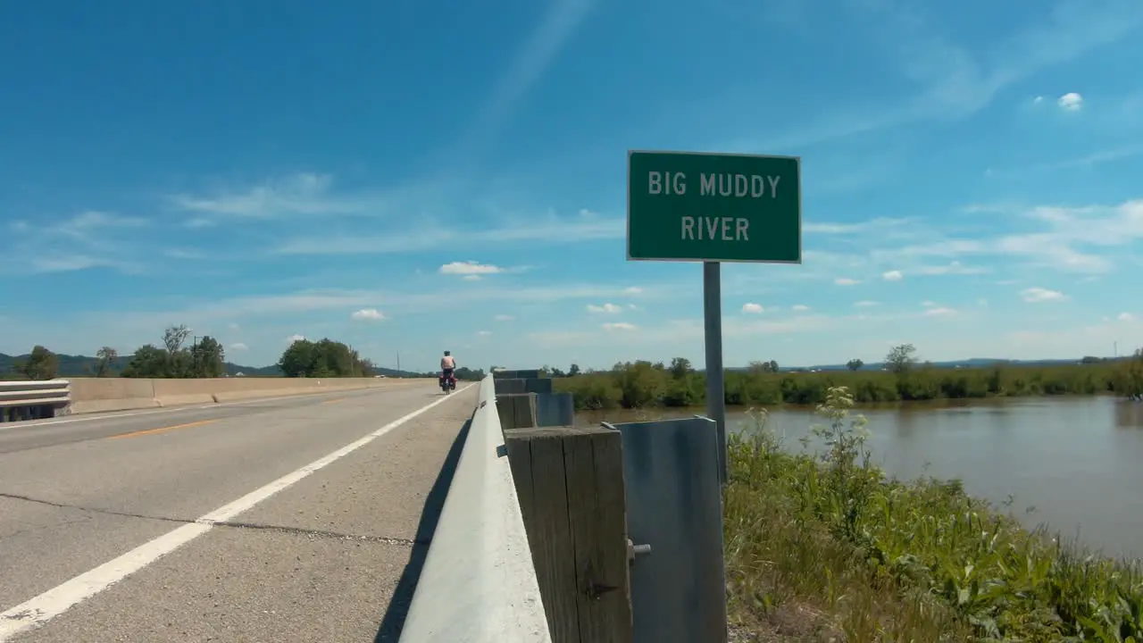 Cyclist bikepacking across bridge over river still shot