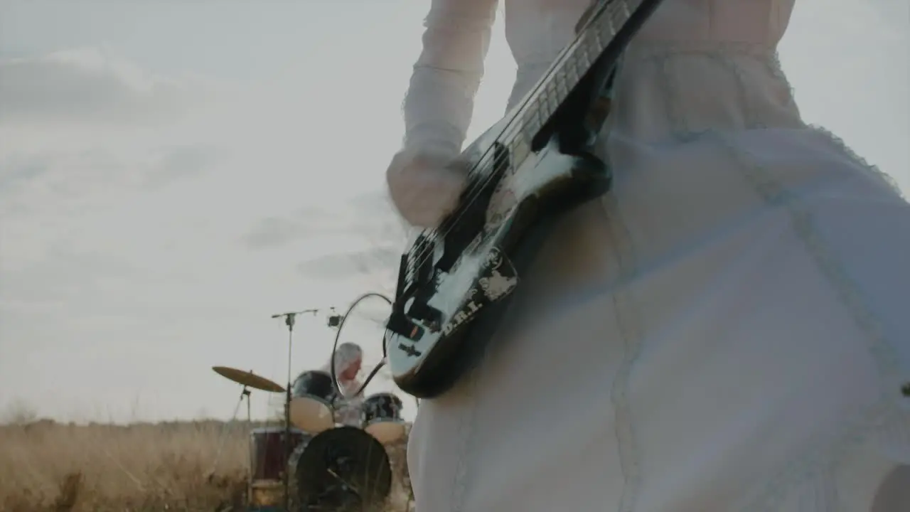 Punk playing bass in wedding dress while drummer is playing in the background in desert