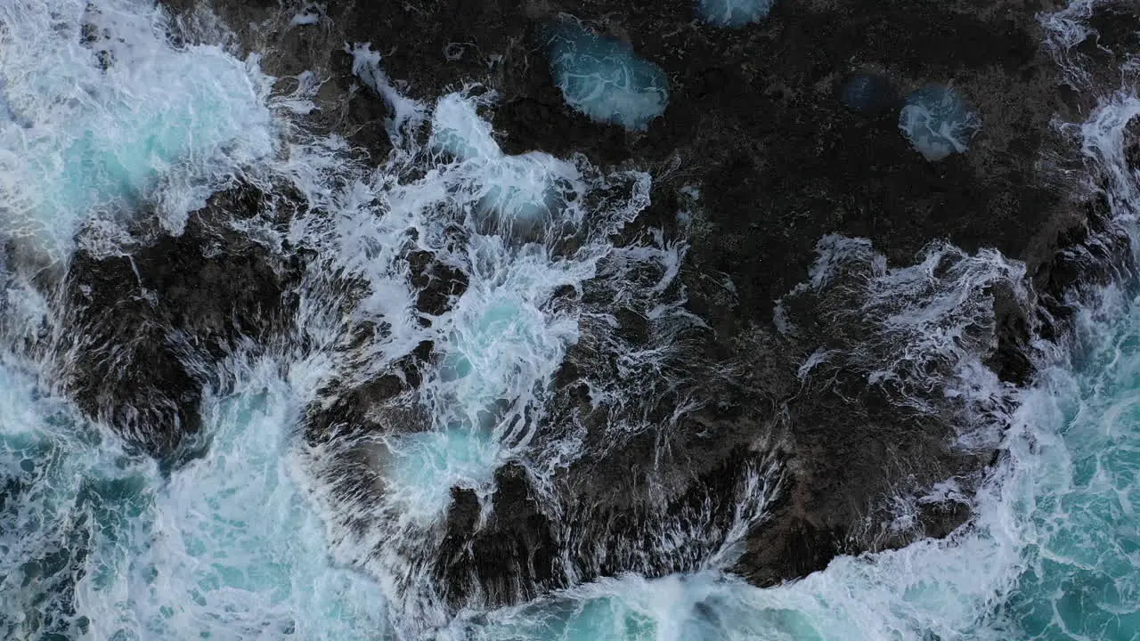 Aerial zoom in as waves crash against a rocky coastline