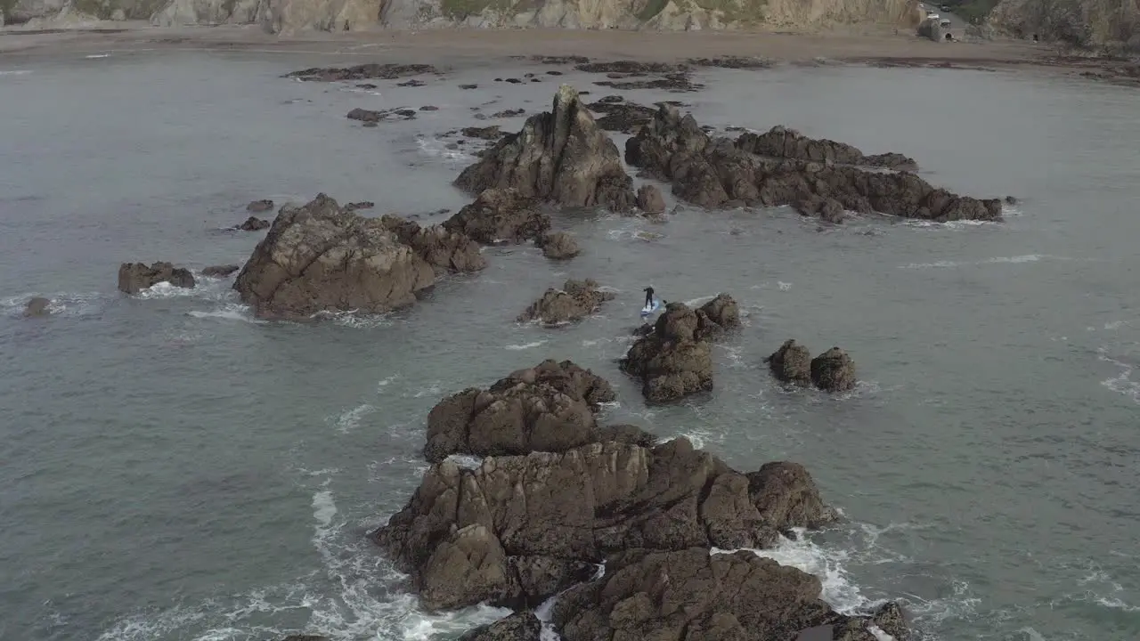 Aerial of skillful SUP paddleboarder paddling among craggy ocean rocks