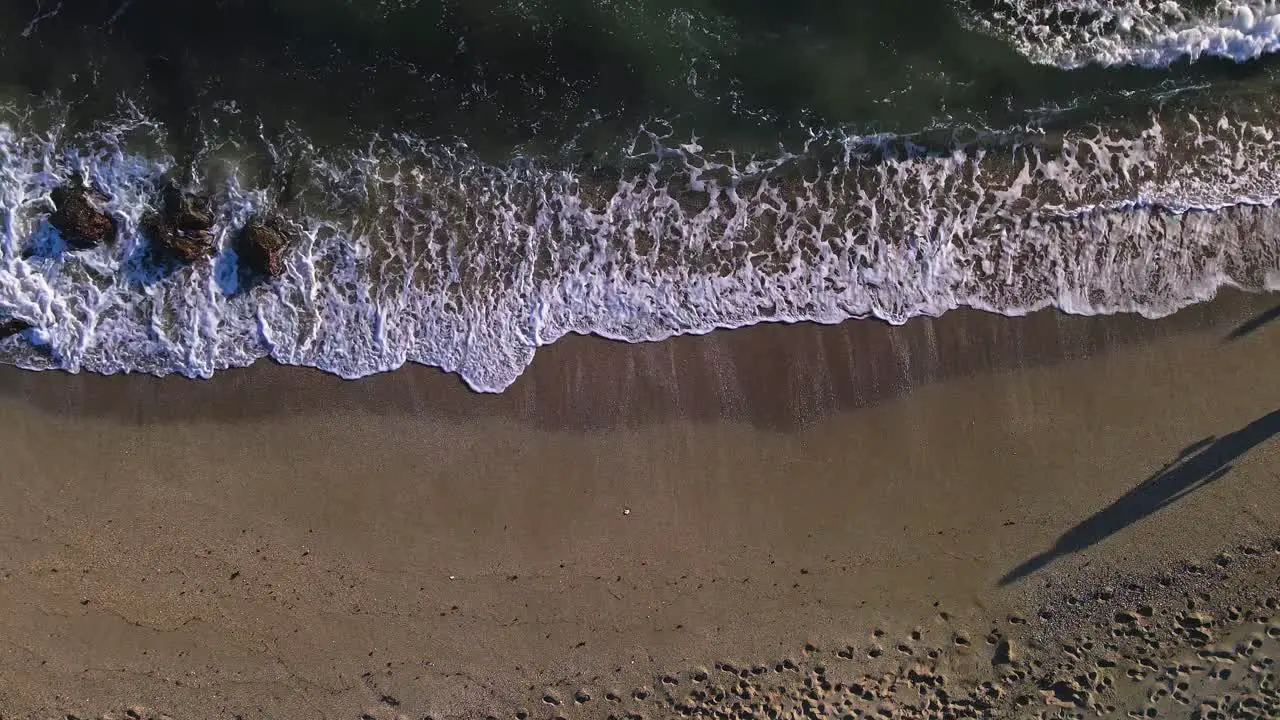 Aerial view of beach waves with a couple of people passing by