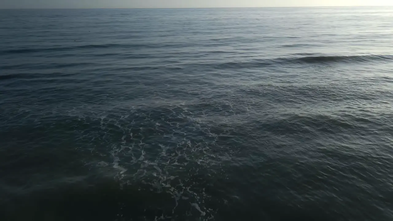 Aerial view of empty beach tilting up into the horizon and moving forward