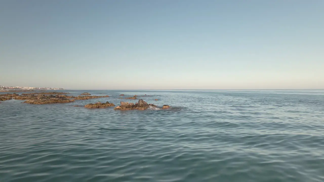 Low angle aerial flying over rugged rocky coast beach out across sunny seascape