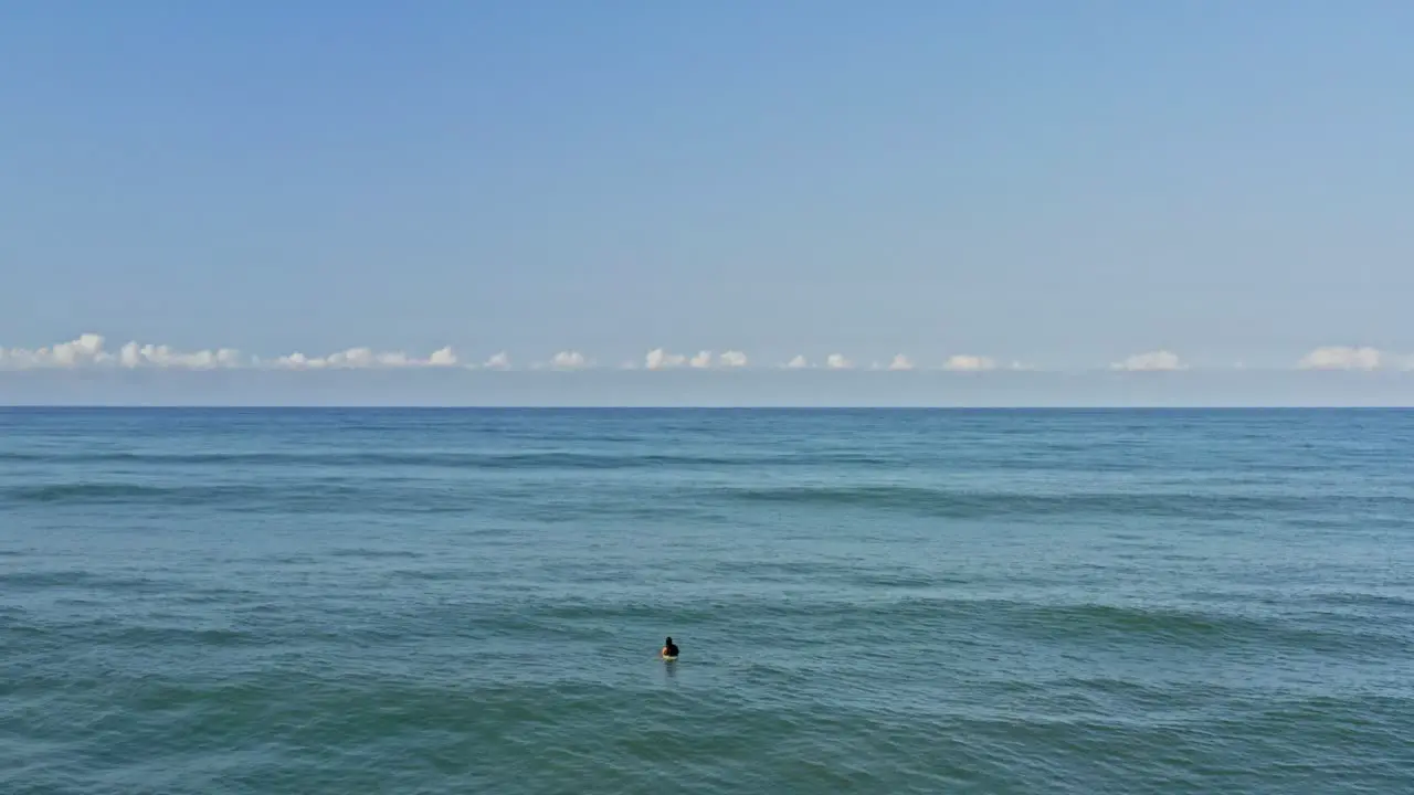 Aerial surfer waiting for waves on surfboard in tropical blue ocean water and sky