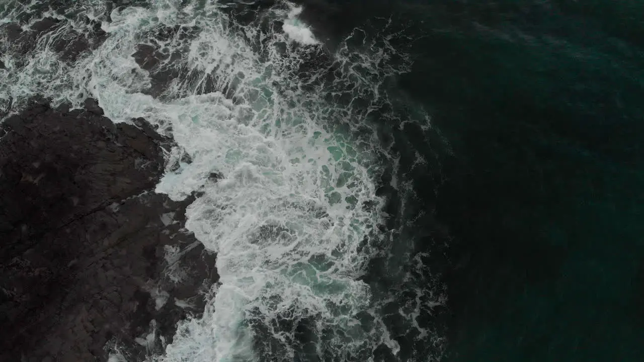 Overhead view of deep aqua marine waves crashing over dark rocks on the west coast of Scotland