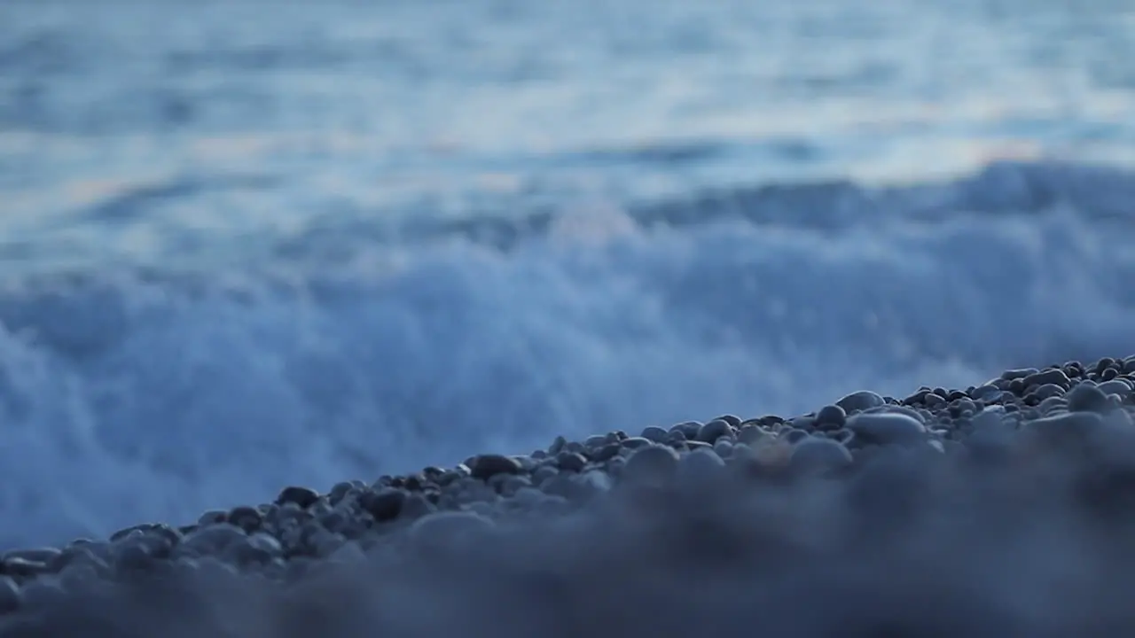 Sea waves splashing and foaming on pebbles beach closeup water shapes in slow motion