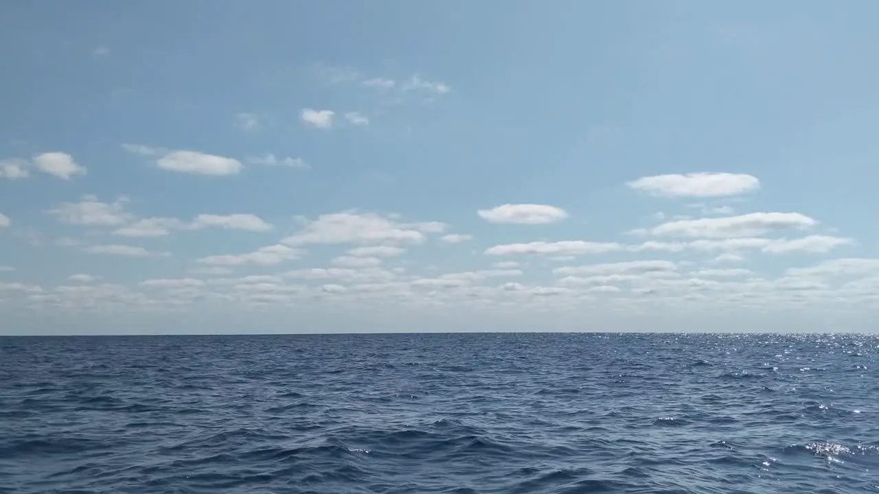 Peaceful panorama view of blue open ocean with sun reflection on calm ripple waves and small clouds in the background on a beautiful sunny day